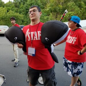 Three members of the PopCult Anime Con staff help unload a truck. The person in front is carrying two big stuffed whales!